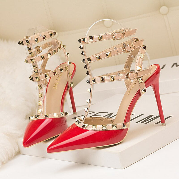 Scarpin salto alto fino com acabamento em verniz, bico fino, tiras com spikes metálicos e fechamento com fivela