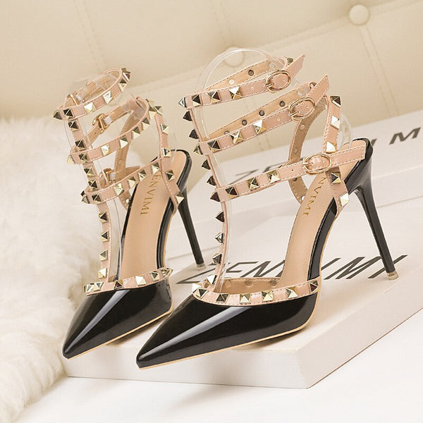 Scarpin salto alto fino com acabamento em verniz, bico fino, tiras com spikes metálicos e fechamento com fivela