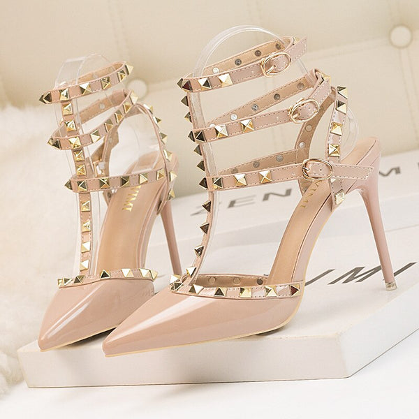 Scarpin salto alto fino com acabamento em verniz, bico fino, tiras com spikes metálicos e fechamento com fivela