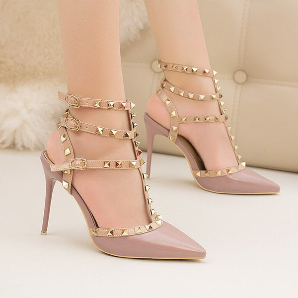 Scarpin salto alto fino com acabamento em verniz, bico fino, tiras com spikes metálicos e fechamento com fivela