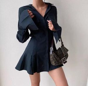 Vestido curto elegante com botões frontais, manga longa, punho estruturado e barra levemente rodada em tecido de alfaiataria premium.